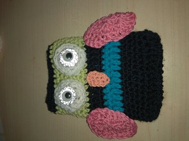 Gehäkelte Monstertasche in Schwarz, Türkis, Hellgrün und Pink mit zwei Kulleraugen auf Holzuntergrund.