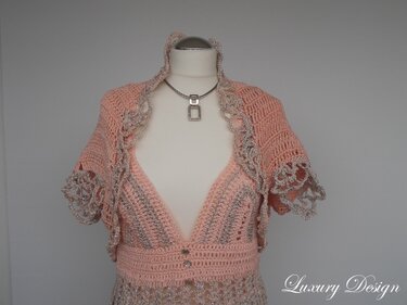 Mannequin trägt pfirsichfarbenes, gehäkeltes V-Ausschnitt-Kleid mit kurzem Bolero und beiger Spitzenkante