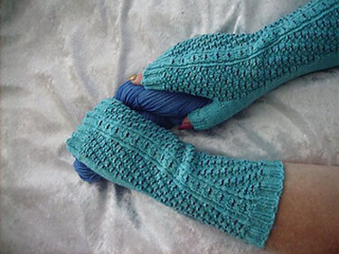 Türkise gestrickte fingerlose Armstulpen mit Daumenöffnung, Hände halten ein Knäuel Garn
