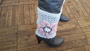 Hellgraue gehäkelte Beinstulpen mit rosa Blüte an dunklen Stiefeletten