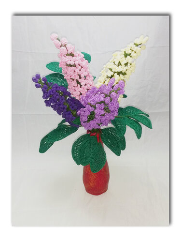 Gehäkelter Strauß mit violetten, rosa und cremefarbenen Blüten sowie großen grünen Blättern in roter Vase