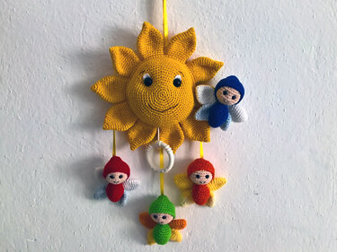 Gehäkeltes Mobile: gelbe Sonne mit lächelndem Gesicht und vier bunten Engelchen