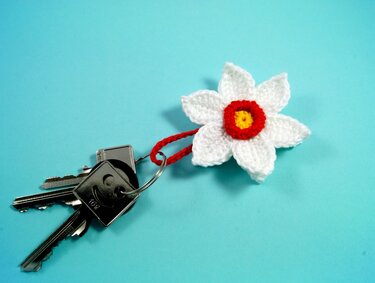 Schlüssel mit gehäkelter weißer Blume mit gelbem Kern und rotem Ring auf blauem Hintergrund
