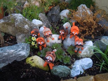 Mehrere kleine gehäkelte orange-braune Katzen-Amigurumi mit Schnurrhaaren und Schwänzen auf Steinen