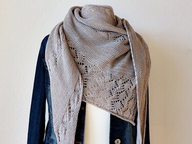 Light-taupe asymmetrical knitted lace shawl on a mannequin showing lace panels and drape