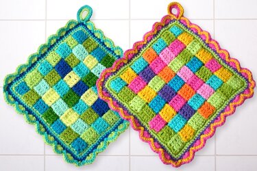 Two crocheted square potholders: one blue/green/yellow and one multicolored; both have ruffled edges and hanging loops.