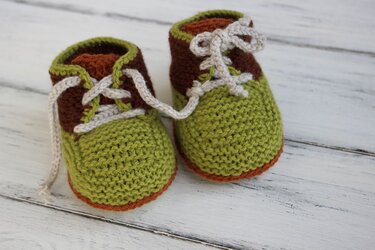 Kleine gestrickte Babyschnürschuhe grün-braun mit hellen Schnürsenkeln auf hellem Holz