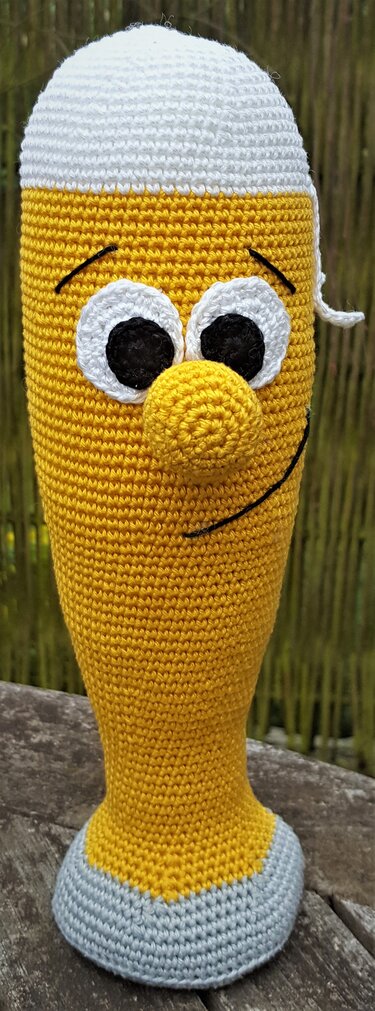 Fröhliche gelbe Amigurumi-Figur mit großen weißen Augen, aufgestickten schwarzen Gesichtszügen und runder Nase