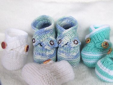 Eine Auswahl an gestrickten Babyschuhen in verschiedenen Farben und Strickarten, teils mit Wickelverschluss und Knöpfen.