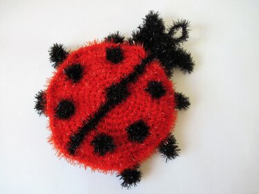 Gehäkelter roter Marienkäfer mit schwarzen Punkten und Fühlern auf hellem Hintergrund.