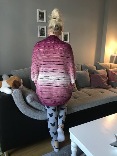 Rückenansicht einer Person auf einem Sofa in einem rosé-weiß verlaufenden, gehäkelten Seelenwärmer