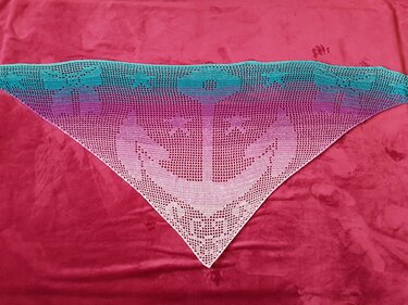 Gehäkeltes dreieckiges Tuch mit Ankermotiv und Farbverlauf von Türkis zu Rosa auf rotem Hintergrund.