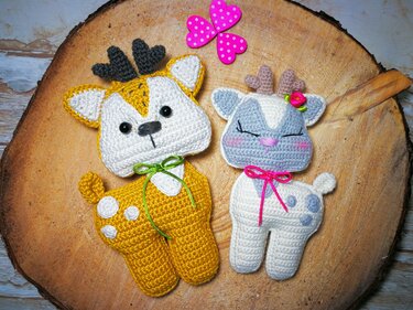 Zwei gehäkelte Amigurumi‑Rehe (senfgelb und weiß‑hellgrau) auf Holzscheibe