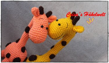 Zwei handgehäkelte Amigurumi-Giraffen, eine gelbe und eine orange, mit braunen Punkten und schwarzen Augen