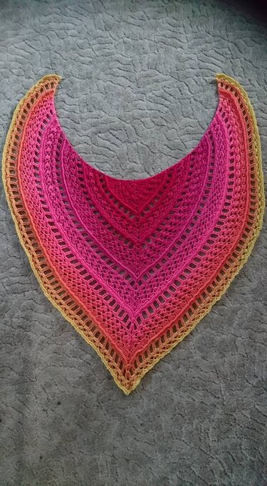 Gehäkeltes Dreieckstuch mit Farbverlauf Pink–Orange–Gelb und offenem Spitzenmuster auf grauem Untergrund