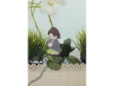 Gehäkeltes Amigurumi‑Engelchen mit braunem Haar auf Pflanzenblatt