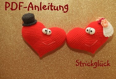 Zwei rote Amigurumi-Herzen, eines mit Zylinder, das andere mit Schleier und Blüten, vor goldenem Glitzerhintergrund; Schriftzug ‚PDF-Anleitung‘