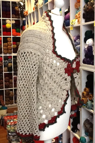 Hellbeige Damen-Strickjacke mit Lochmuster und roten Zierkanten auf einer Schneiderpuppe