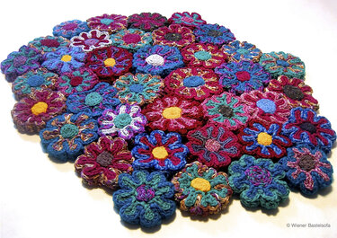 Dicht angeordnete handgehäkelte Blüten in Blau-, Rot- und Grüntönen