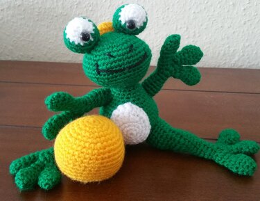 Gehäkelter grüner Frosch-Amigurumi mit weißem Bauch und gelber Kugel