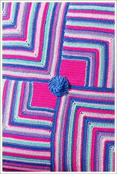 Gehäkelter Stoff in Pink, Blau, Mint und Violett mit konzentrischen Quadraten und rundem blauen Zierelement.