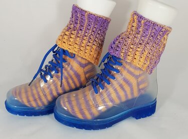 Transparente Stiefel mit blauer Sohle und blauen Schnürsenkeln, darin gestreifte lila-orange Socken und gemusterte Beinstulpen