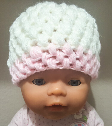 Gehäkelte Babymütze mit Puff-Stich-Muster in Weiß und Rosa auf einer Puppe.