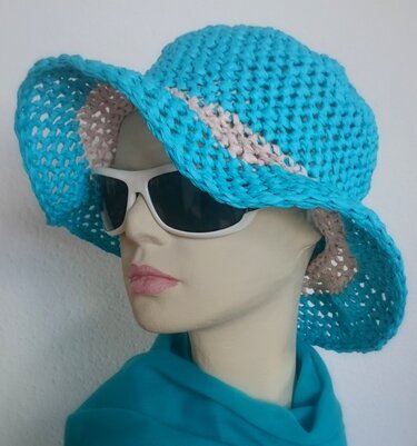Türkis gehäkelter Sonnenhut mit breiter Krempe und beigem Streifen auf Schaufensterpuppe mit weißer Sonnenbrille