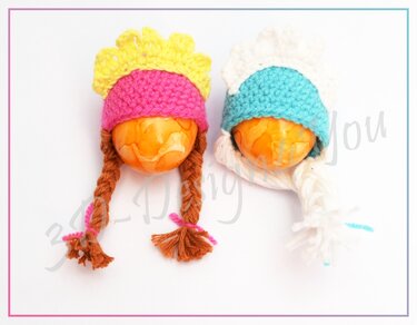 Nahaufnahme zweier gehäkelter Eierwärmer mit Bündchen und geflochtenen Zöpfen in unterschiedlichen Farbkombinationen