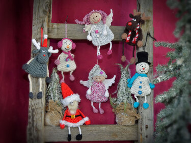 Gehäkelte Amigurumi-Weihnachtsanhänger (Rentier, Schneemann, Engel, Weihnachtsmann) an Holzleiter vor rotem Hintergrund