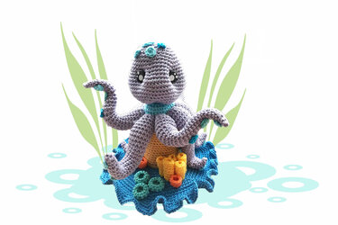 Gehäkelter lila Oktopus-Amigurumi mit türkisfarbenen Akzenten, blauer Basis und gehäkelten Korallen
