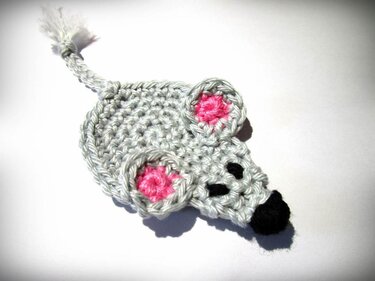 Gehäkelte graue Maus-Applikation mit rosa Innenohren und schwarzer Nase auf weißem Hintergrund