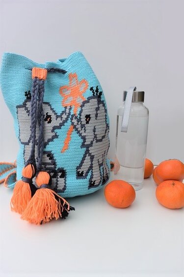 Türkis gehäkelter Beutelrucksack mit zwei grauen Elefanten, orangefarbenen Quasten; daneben Mandarinen und eine Wasserflasche.