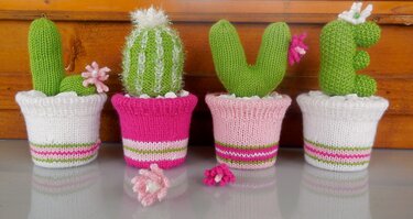 Vier verschieden geformte gestrickte Kakteen in gestreiften Töpfen