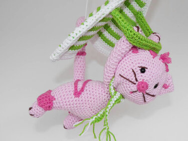 Rosa gehäkelte Amigurumi-Katze mit grün-weiß gestreiftem Halter und grünem Schal