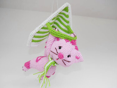 Gehäkelte rosa Amigurumi-Katze mit grün-weiß gestreiftem Hut und Schal.