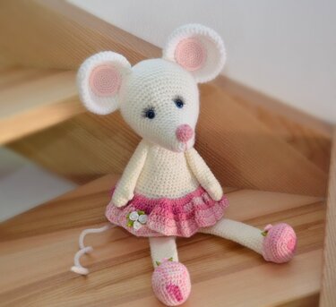 Gehäkelte weiße Maus mit rosa Stufenkleid und rosa Schuhen sitzt auf Holzstufen