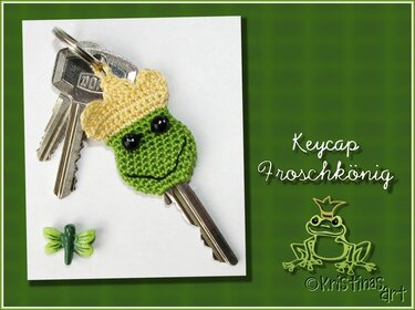 Gehäkelte grüne Schlüsselkappe in Froschkönig-Form mit gelber Krone an einem Schlüssel, daneben eine kleine grüne Libellen-Dekoration