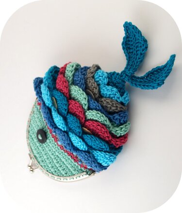 Gehäkelte Fischtasche mit bunten, geflochtenen Schuppen, gehäkelter Schwanzflosse, Knopfauge und Metallklapprahmen auf weißem Hintergrund.