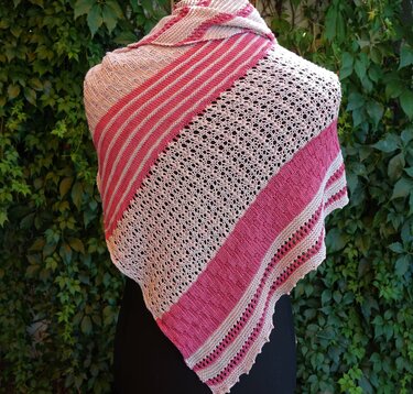 Gestricktes Dreieckstuch rosa und creme mit Streifen und Ajourmuster, auf einem schwarzen Oberteil vor grünem Blatthintergrund drapiert