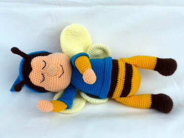 Gehäkelte Amigurumi-Biene mit blauem Oberteil und gelb-braun gestreiftem Körper auf hellem Hintergrund