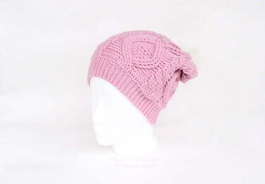 Rosafarbene gehäkelte Beanie mit Zopfmuster auf weißem Mannequinkopf.