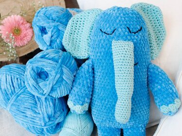 Blauer gehäkelter Amigurumi‑Elefant mit langem Rüssel neben blauen Garnknäueln