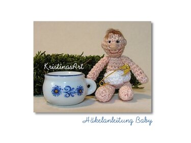 Gehäkelte Mini-Babypuppe mit weißer Windel und Sicherheitsnadel neben kleinem Porzellantässchen