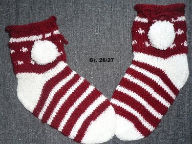 Zwei gestrickte Babysocken in Rot und Weiß mit Streifenmuster und weißen Bommeln, Größe 26/27.