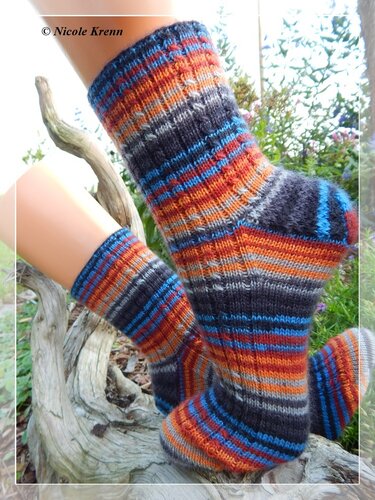 Gestrickte Ringelsocken in Grau, Orange und Blau auf einem Holzstück