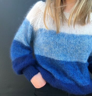 Woman wearing a fuzzy blue and white striped knitted pullover with ribbed cuffs.