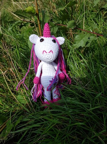 Gehäkeltes weißes Einhorn mit pink‑lila Mähne im Gras