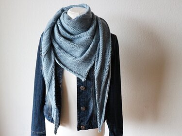 Triangular knit shawl draped over a denim jacket on a mannequin showing length and point placement
