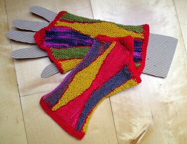 Bunte handgestrickte fingerlose Handschuhe mit Streifen auf Holzuntergrund